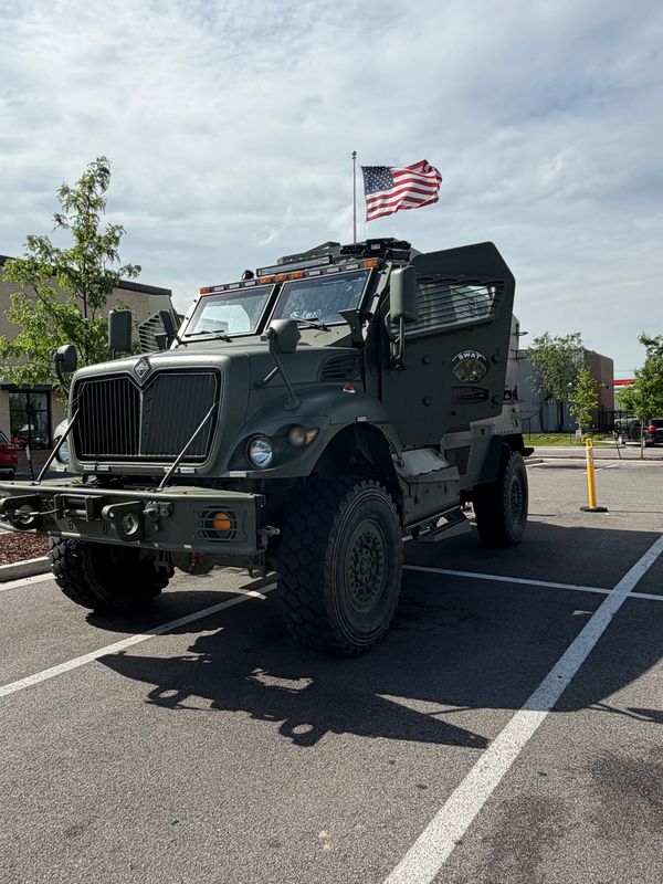 Military vehicle with American flag on top parked in lot.