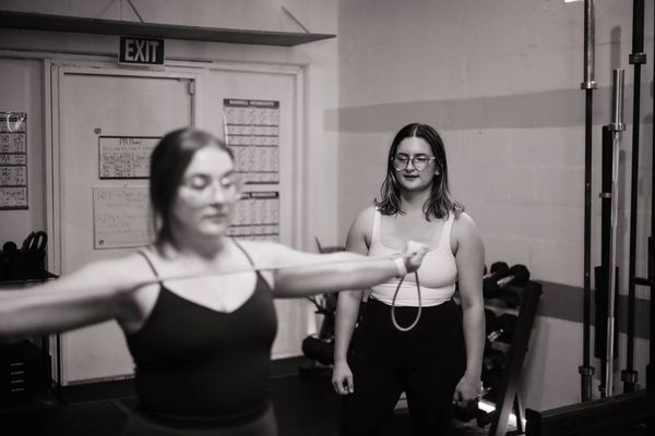 Two women exercising in a gym, one using a resistance band.