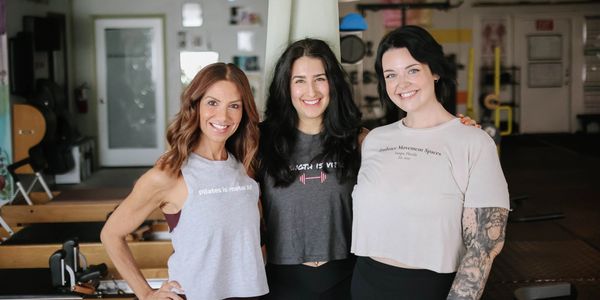 Three women smiling together in a gym setting.