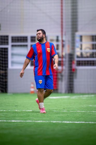 Homem caminhando em campo de futebol com uniforme azul e vermelho.