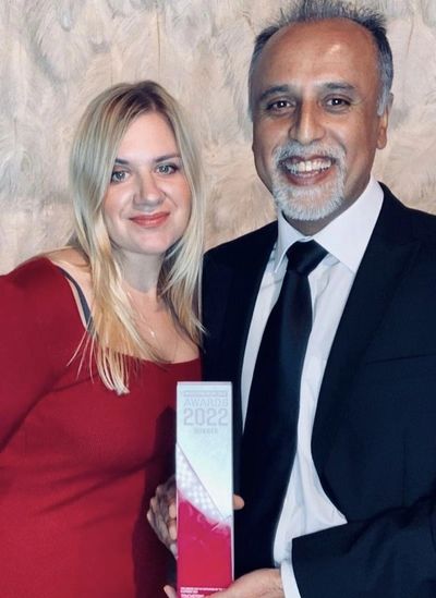 white female woman with Asian male, at an awards ceremony holding an award and smiling.