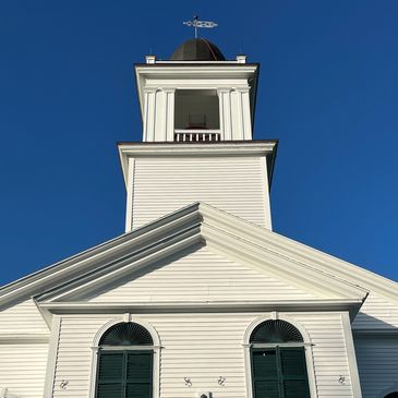 White church building with green shutters under a clear blue sky.