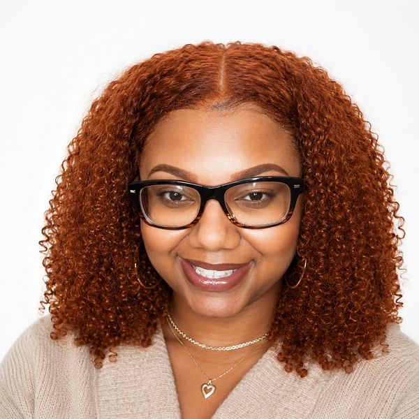 Smiling woman with curly red hair and glasses.