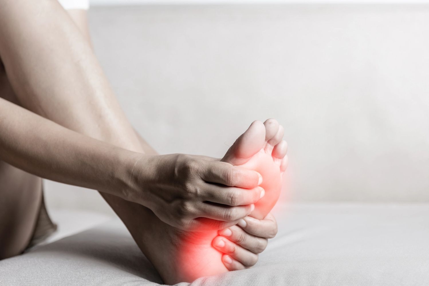 Person holding their foot with red highlighting pain areas.