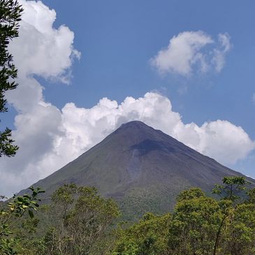 Mountain peak with clouds and trees under a blue sky.