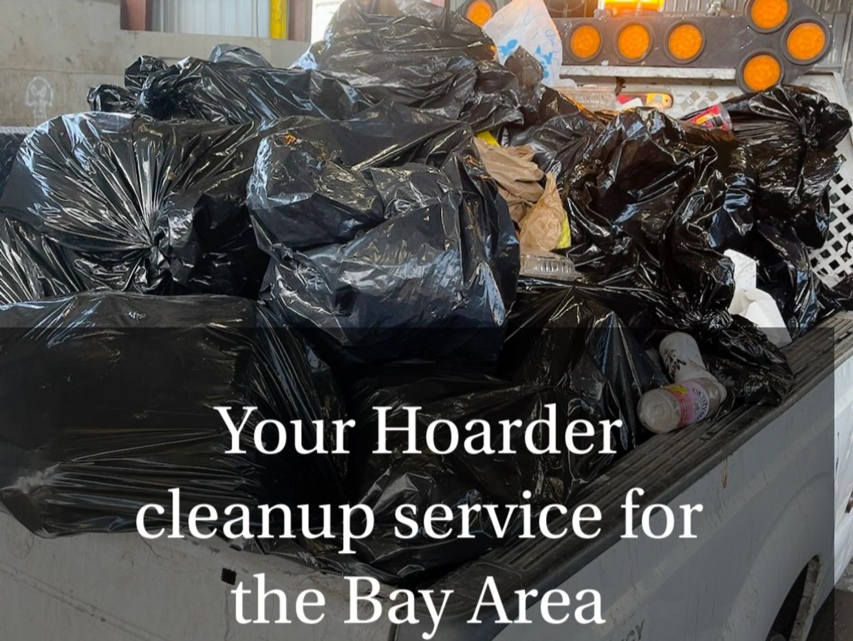 A man in overalls and a face mask cleaning up a pile of debris in a driveway with a truck trash bags