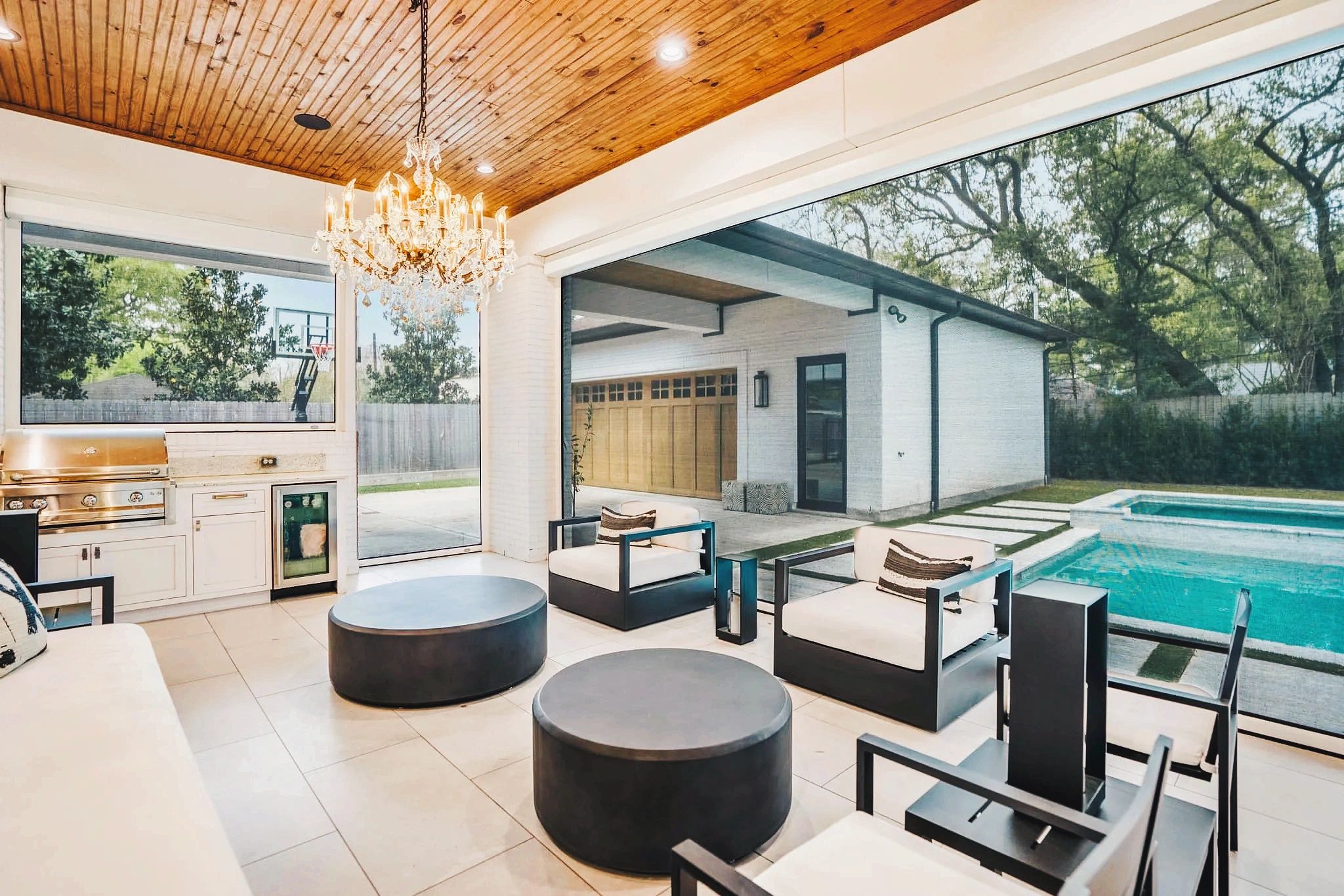 An outdoor kitchen with chandelier opens onto a poolside patio with three motorized screens.