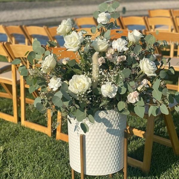 Elegant white floral arrangement in a textured white vase on a stand.