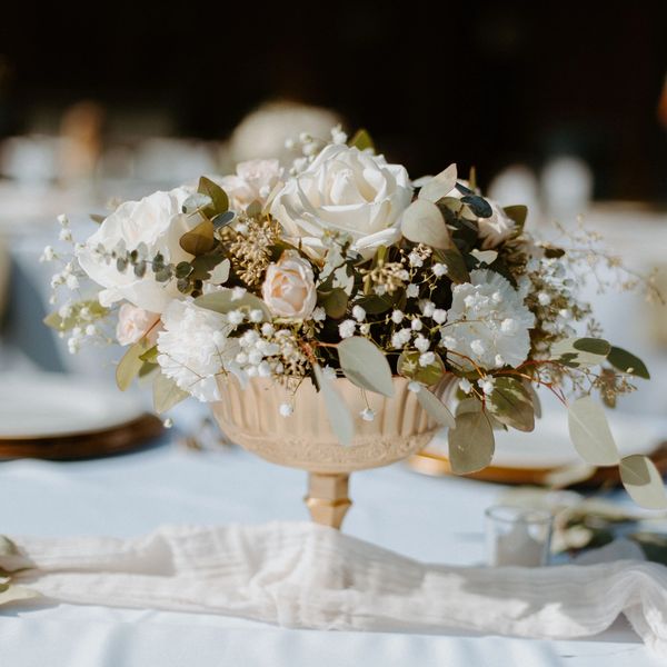 Elegant floral centerpiece with white roses and greenery on a table at an outdoor event.