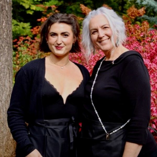 Bride in a white wedding dress with a black jacket, standing outdoors on grass.
