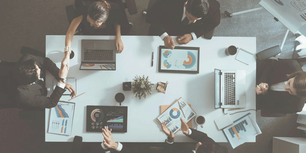Business meeting with professionals discussing charts and shaking hands around a table.