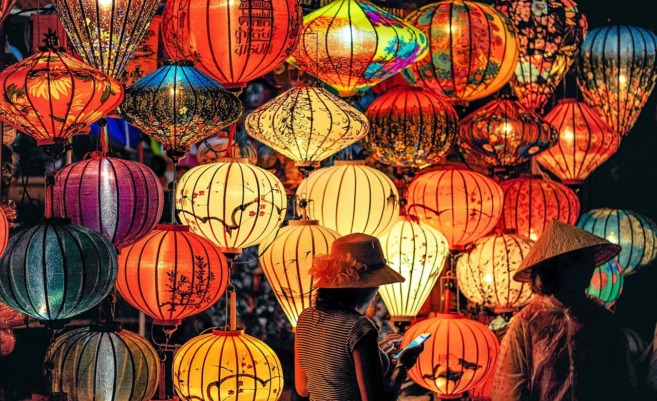 This vibrant image captures a scene of cultural allure, featuring a colorful array of traditional Asian lanterns. The intricate designs and warm glow of the lanterns create a captivating ambiance, while figures wearing conical hats add to the authentic atmosphere, suggesting a festive or market setting rich in tradition and craftsmanship. This picturesque scene is typical of lantern festivals or night markets, often found in East Asian countries, where such lanterns are not just sources of light but also works of art symbolizing joy and good fortune. This vibrant image captures a scene of cultural allure, featuring a colorful array of traditional Asian lanterns. The intricate designs and warm glow of the lanterns create a captivating ambiance, while figures wearing conical hats add to the authentic atmosphere, suggesting a festive or market setting rich in tradition and craftsmanship. This picturesque scene is typical of lantern festivals or night markets, often found in East Asian countries, where such lanterns are not just sources of light but also works of art symbolizing joy and good fortune.