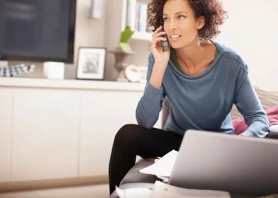 Woman calling a therapist while using a laptop, representing virtual therapy appointment scheduling