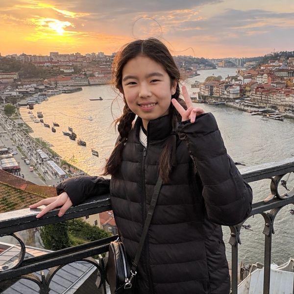 Girl showing peace sign by a river at sunset.
