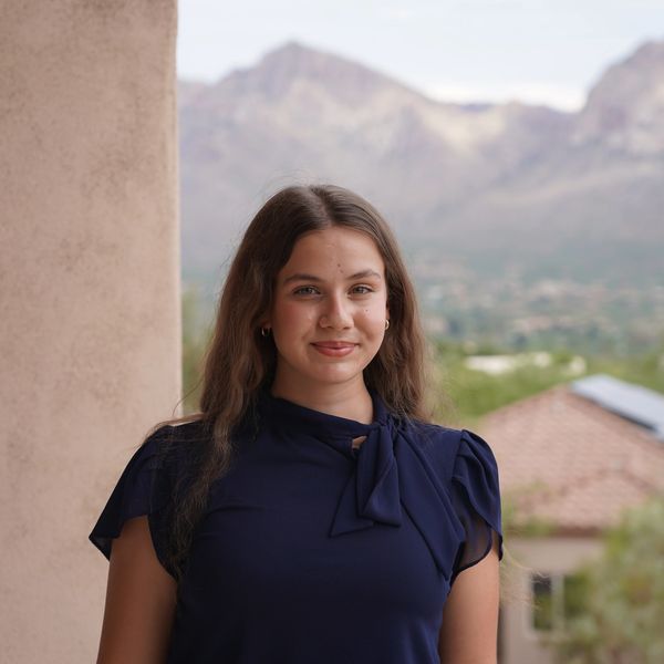 Young woman smiling outdoors with mountains in the background.