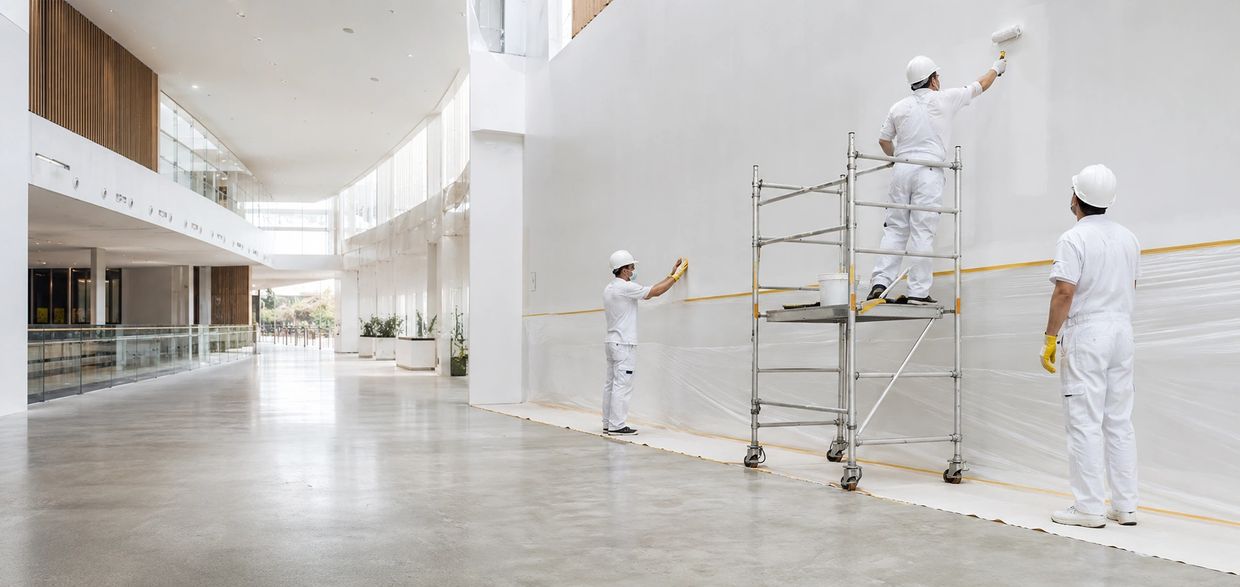 Workers painting a large indoor white wall.