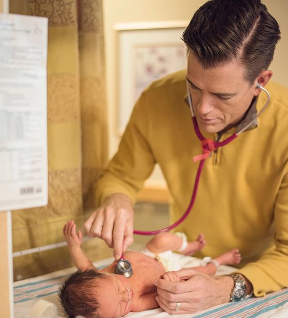 Pediatrician using stethoscope to examine sick baby receiving oxygen