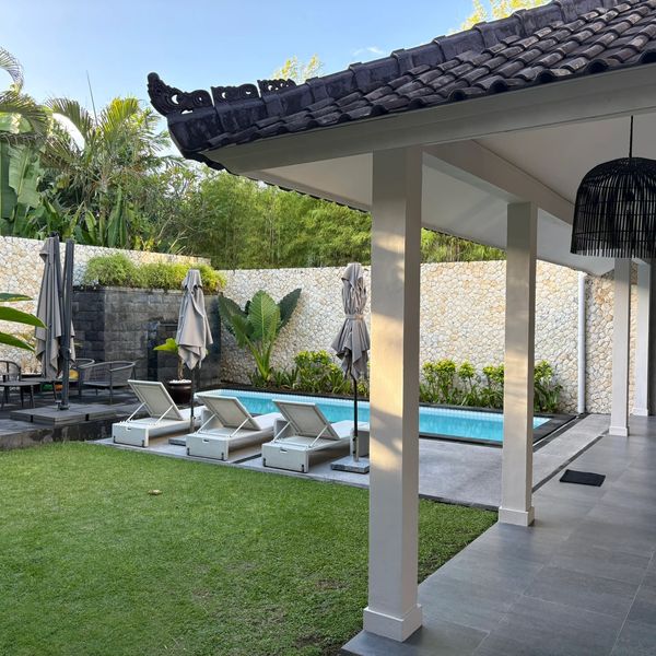 Outdoor pool area with lounge chairs and umbrellas beside a covered patio.