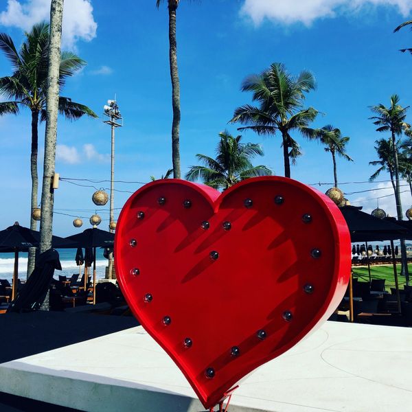 Large red heart decoration against a tropical beach backdrop.