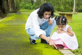 Madre de la India mostrándole a su hija una plantita en un jardín.