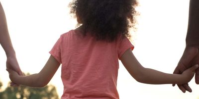 A child holding her parents' hands as they walk together.