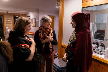 Three women chatting indoors, one wearing a red hijab.