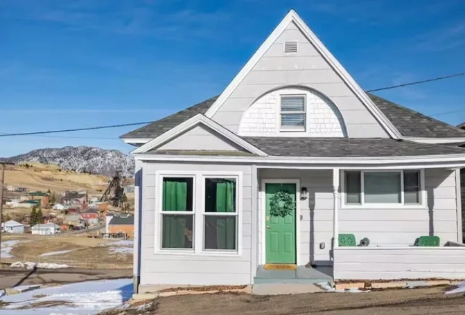 Charming cottage with green door, set against a backdrop of hills and historic mining town.