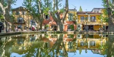 Colorful buildings reflected in a calm pond surrounded by trees.