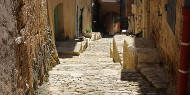 Sunlit narrow cobblestone alley between old stone buildings.