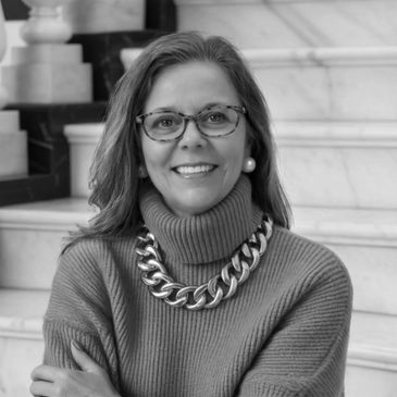 Woman with glasses and chunky necklace smiling on stairs.