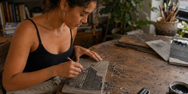 Woman carving a building design onto a wooden block.