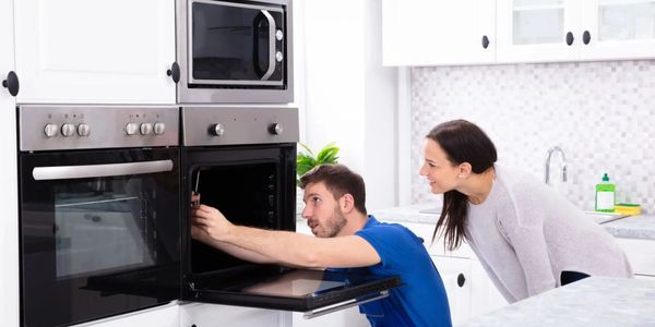 Technician fixing built-in oven as homeowner watches—trusted appliance repair right in your kitchen.