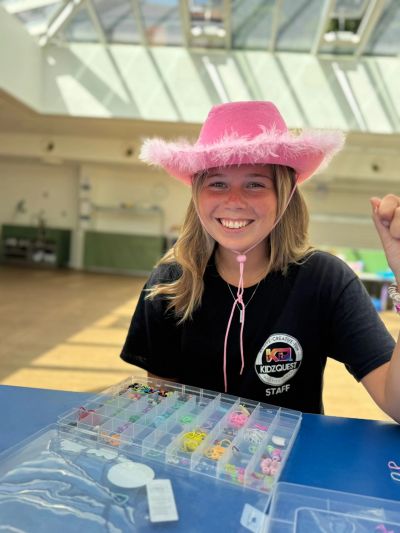 Smiling girl wearing a pink hat and crafting beads.