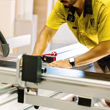 Worker measuring wood panel with tape measure in workshop.