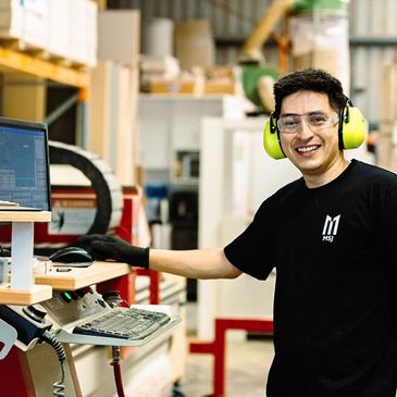 Man in safety gear working on computer in industrial setting.