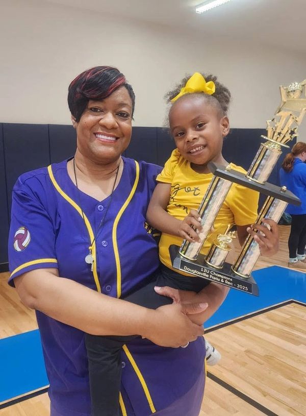 Woman and child proudly holding a sports trophy in a gym.