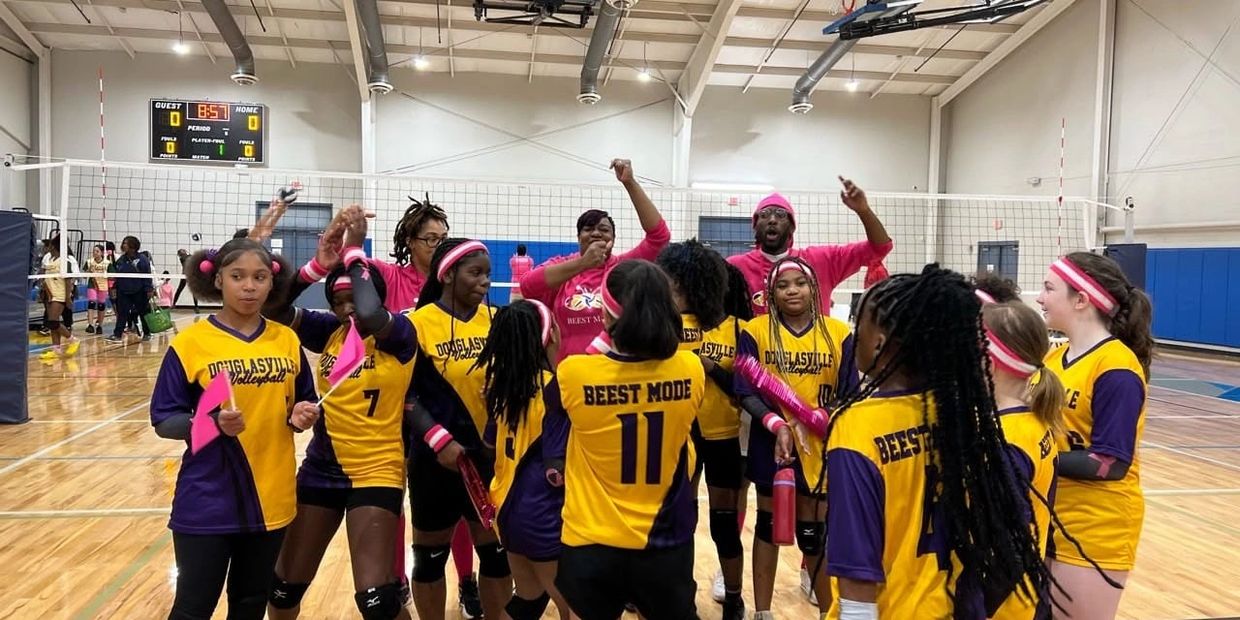 Youth volleyball team in yellow and purple uniforms celebrating in a gymnasium.