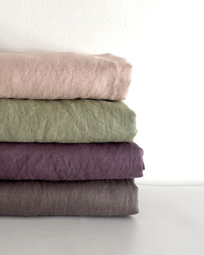 Folded French linen sheets stacked neatly in natural, sage, amethyst, and lilac gray colors.
