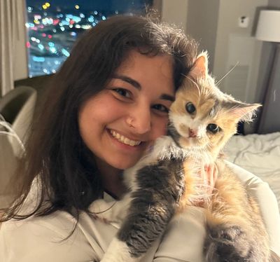 A woman smiling while holding a fluffy calico cat.