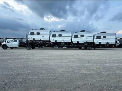 Four trailers loaded on a flatbed truck under a cloudy sky.