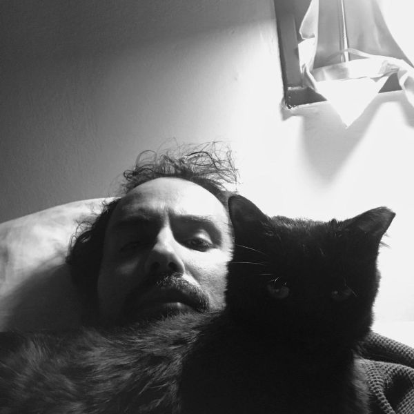 Man lying with a black cat close to his face in black and white.