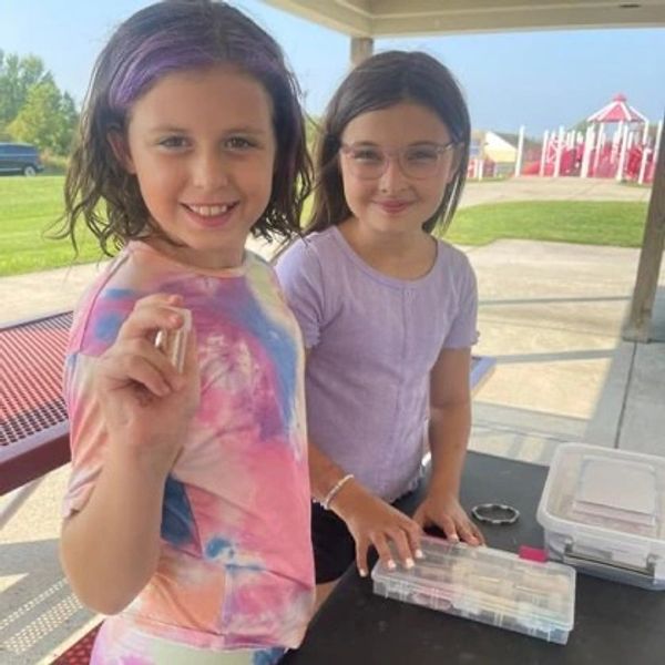 Two young girls smiling by a table outdoors.