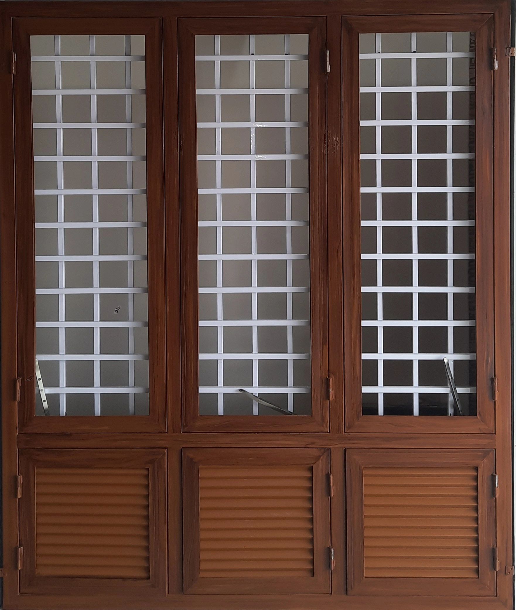 Wooden window with white grid bars and louvered shutters.