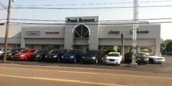 Car dealership with multiple parked vehicles and brand signs on the building.