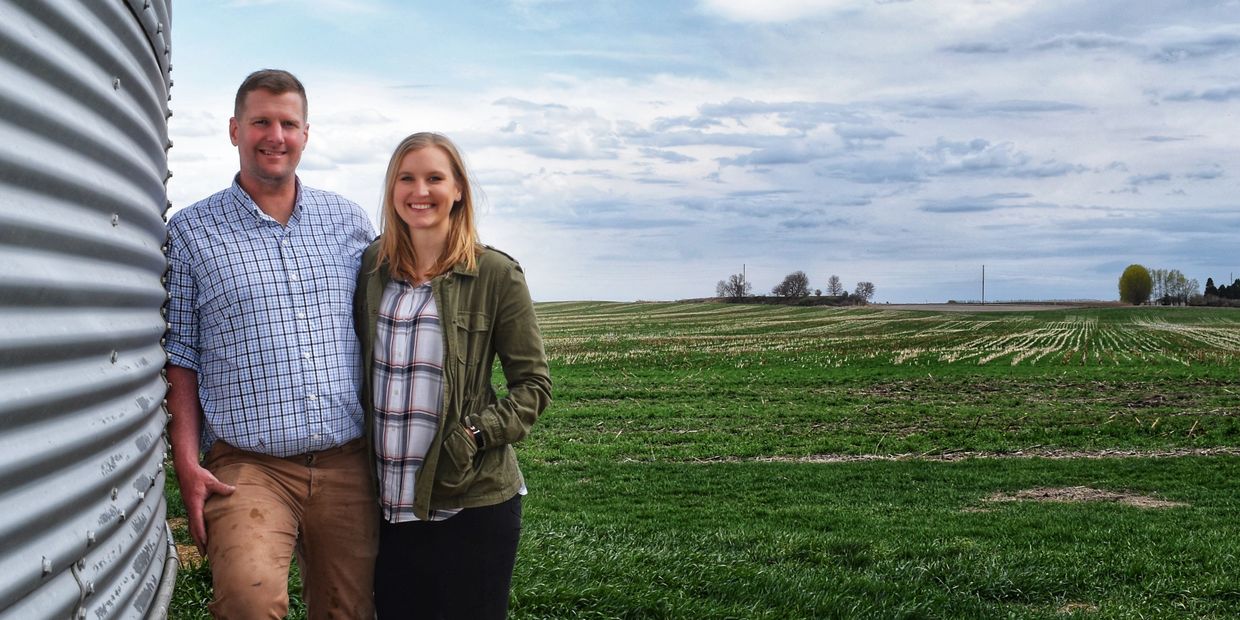 Happy couple standing by a metal silo in a green field.