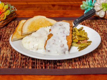 Fried chicken with gravy, green beans, and toast on a white plate.