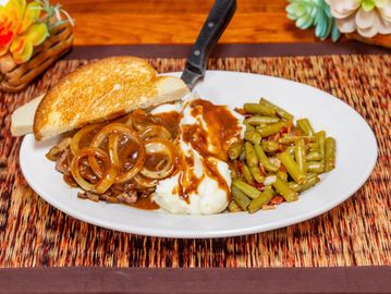 Plate with meal of mashed potatoes, green beans, beef burger patty with onions and gravy, and bread.
