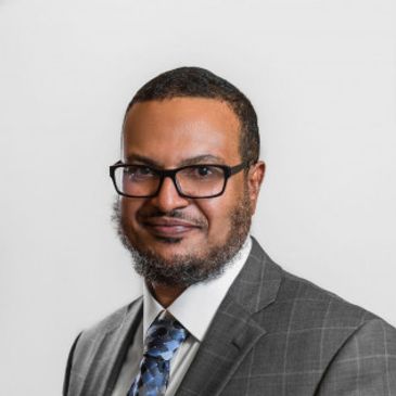 A professional man in a gray checked suit and glasses.