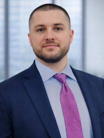 Professional man in a suit and purple tie posing for a headshot.