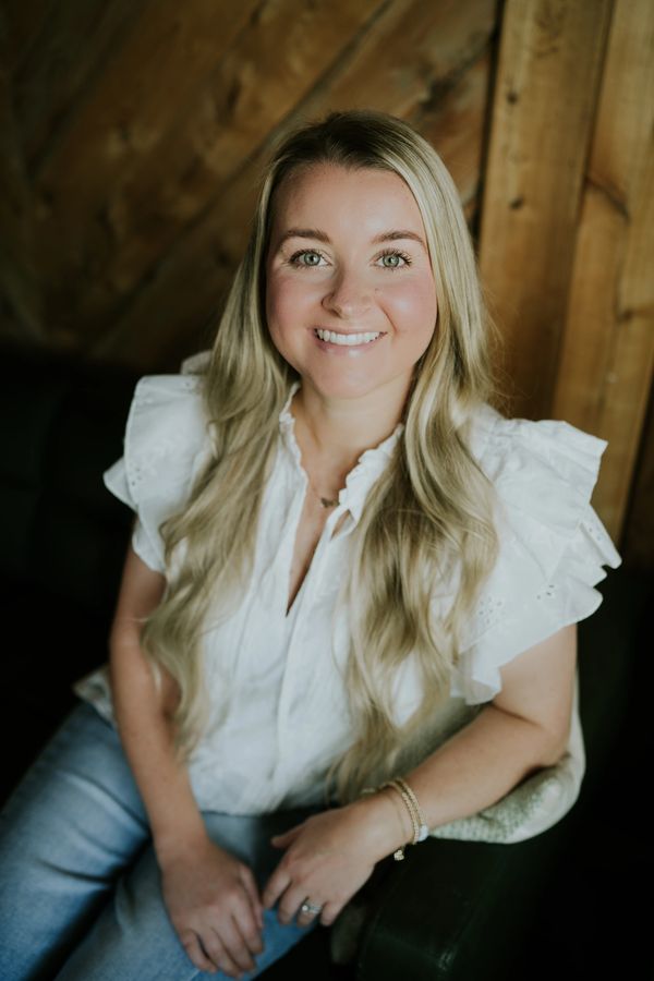 Smiling woman with long blonde hair sitting on a chair.